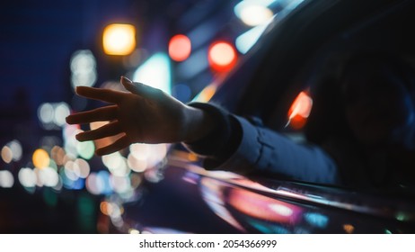 Female is Commuting Home in a Backseat of a Taxi at Night. Passenger Chilling and Holding Her Hand Outside of Window while in a Car in Urban City Street with Working Neon Signs.