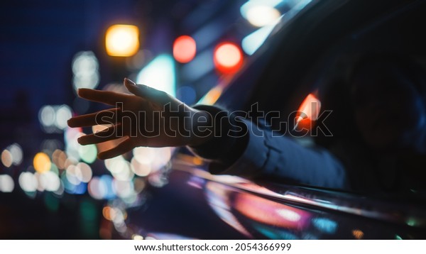 Female is\
Commuting Home in a Backseat of a Taxi at Night. Passenger Chilling\
and Holding Her Hand Outside of Window while in a Car in Urban City\
Street with Working Neon\
Signs.