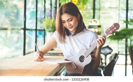 Female Composer Is Writing Music In A Joyful Feeling Using Ukulele As A Device In The Vintage-style Café, Soft Tone Vintage Style