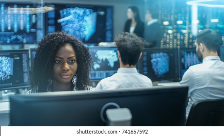 Female Computer Engineer Works On A Neural Network/ Artificial Intelligence Project With Her Multi-Ethnic Team Of Specialist. Office Has Multiple Screens Showing 3D Visualization.