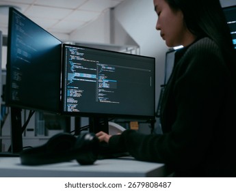 Female Computer Programmer working on Computer Writing and Developing Software Program, App looking at Dual screens in Creative Office workspace. Focused Professional female software developer work.