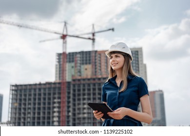 Female construction engineer. Architect with a tablet computer at a construction site. Young Woman looking, building site place on background. Construction concept - Powered by Shutterstock