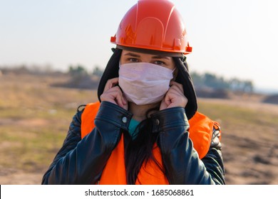 Female Construction Worker In Overalls Putting On Medical Mask On Face On Construction Area.