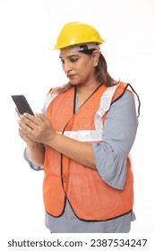Female constructor using cell phone. Wearing hardhat and worker apron while isolated on white studio background.