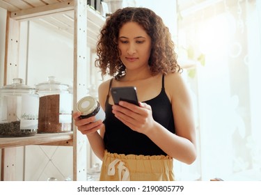 Female Consumer Or Customer With Phone Searching Organic Product Information Online For Ethical, Vegan Or Healthy Ingredients. Eco Conscious Buyer Reading Label Locally Made Coffee Grain Jar In