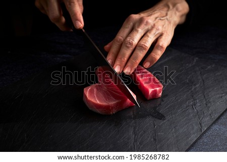 Female cook preparing a piece of bluefin tuna to make sushi on a blackboard. Asian food concept