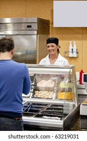 Female Cook Waiting For A Student To Choose His Lunch In The Cafeteria