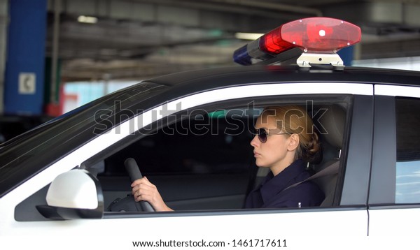 Female cop driving police car in underground\
parking, patrolling, law and\
order