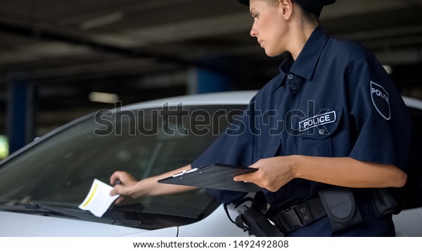 Female cop putting traffic ticket for parking\
violation on windshield,\
fine