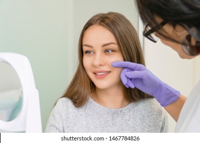 Female cosmetologist showing to young smiling woman the face zones to apply clinic treatment. Medicine, aesthetic and beauty clinic