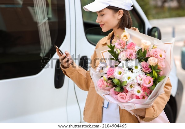 Female courier with bouquet of flowers and phone\
near car outdoors