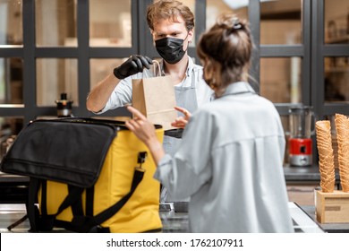 Female Courier Taking Online Order For Delivery At The Counter With Salesperson In The Small Pastry Shop Or Cafe. Concept Of A Take Away Food During Pandemic