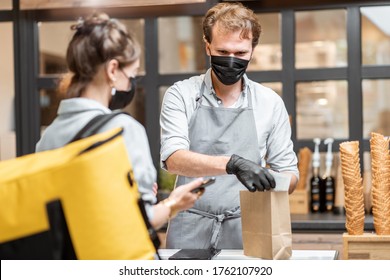 Female Courier Taking Online Order For Delivery At The Counter With Salesperson In The Small Pastry Shop Or Cafe. Concept Of A Take Away Food During Pandemic