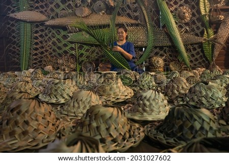 female craftsman weaving handmade Thai traditional hat basketry from palm leaf at rural village in Amphawa, Samutsongkhram province, Thailand