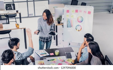 Female Creative Director Team Lead Brainstrom Branding Project With Designer Team Hand Up To Ask Question At Meeting Table.discussion Idea In Creative Office