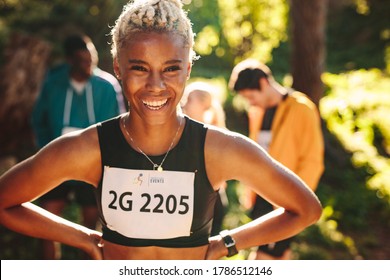 Female Cross Country Marathon Runner Smiling Outdoors. Sportswoman Laughing Outdoors With Her Club Members In Background.