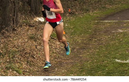 A female cross country runner is racing in the woods trying to hold on to first place at a high school race.