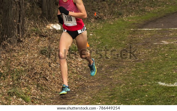 A female cross\
country runner is racing in the woods trying to hold on to first\
place at a high school race.
