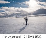 Female cross-country skiier skiing in a flat windswept terrain in a partly hidden groomed track in the norwegian mountains at easter