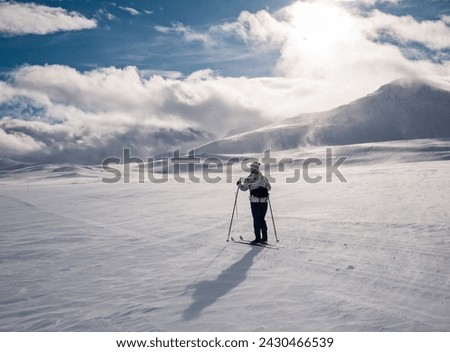 Female cross-country skiier skiing in a flat windswept terrain in a partly hidden groomed track in the norwegian mountains at easter