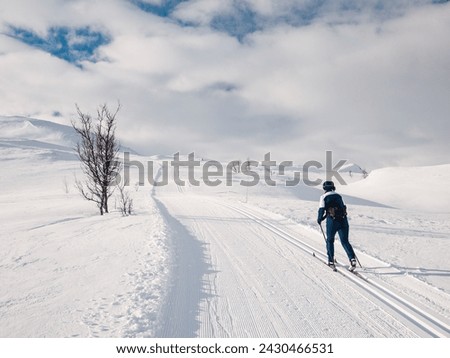 Female cross-country skiier skiing uphill in a groomed track in the norwegian mountains at easter