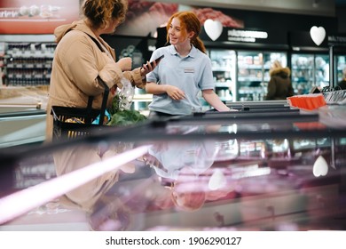 Female Customer Asking Supermarket Worker For Help Finding A Food Item. Woman Holding Her Mobile Phone And Asking For Help To A Female Grocery Store Employee.