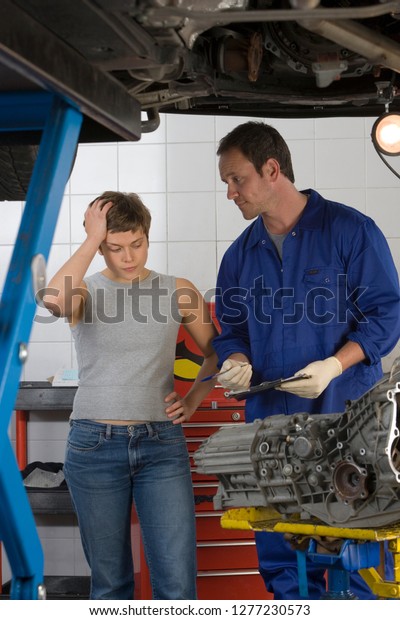 Female customer being shown car repair bill by\
mechanic in garage