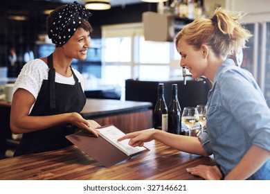 Female customer choosing wine from a wine list being presented to her by a charming young African American bartender in a bar conceptual of employment, small business ownership or an entrepreneur - Powered by Shutterstock