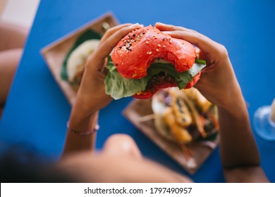 Female Customer Eating Tasty Hearty American Burger With Tomato Bread Rolls And Vegan Meat, Hungry Woman Enjoying Leisure Time For Have Lunch With Delicious Caloric Hamburger During Cheat Meal On Diet