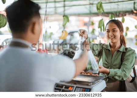 female customer giving the plastic bag that full of fruits to the male seller at cashier