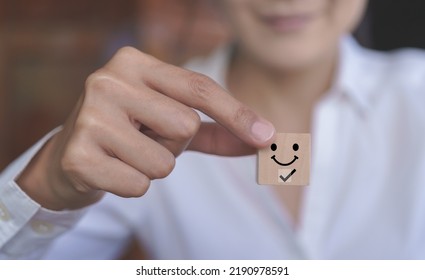 Female customer holding a wooden block smiling face icon. Customer satisfaction evaluation concept, good experience, good review, high score, impressive service.