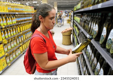 A female customer is interested in the content of olive oil grocery in store, supermarket - Powered by Shutterstock