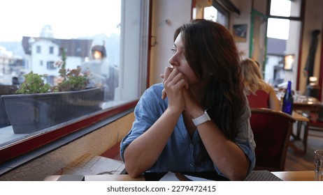 Female customer seated at restaurant staring out window. One contemplative woman at cafe place