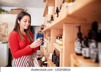 Female Customer Shopping In Independent Cosmetics Store Comparing Prices Using Mobile Phone