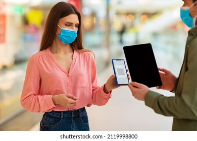 Female Customer Showing Phone With QR Code Of Digital Coronavirus Vaccination Certificate On Screen For Scanning To Male Holding Tablet With Blank Screen Standing Wearing Face Mask In Supermarket - Powered by Shutterstock