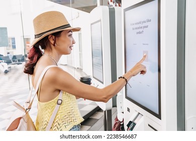 A female customer uses a touchscreen terminal or self-service kiosk to order at a fast food restaurant. Automated machine and electronic payment - Shutterstock ID 2238546687