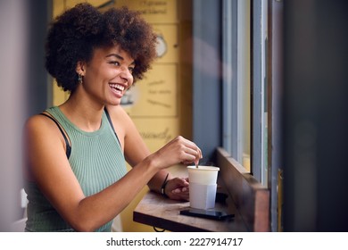 Female Customer In Window Of Cafe Stirring Hot Drink In Takeaway Cup With Wooden Stirrer - Powered by Shutterstock