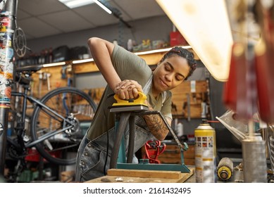 Female Cycling Mechanic Fixing Bike Tube In Bicycle Workshop. Young Concentrated Black Girl With Tattoos. Bike Service, Repair And Upgrade. Garage Interior With Tools And Equipment