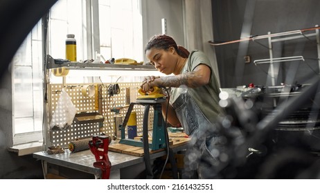 Female Cycling Serviceman Fixing Bike Tube In Bicycle Workshop. Young Concentrated Black Girl With Tattoos. Bike Service, Repair And Upgrade. Garage Interior With Tools And Equipment