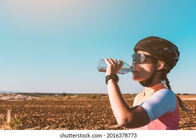 A female cyclist drinks water from a bottle during sunset. Cycling concept. Sport concept. - Powered by Shutterstock