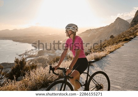 A female cyclist enjoying a beautiful seaside view during sunset amidst her training.Woman cyclist wearing pink cycling kit and white helmet on a gravel bike.Calp,Alicante,Spain