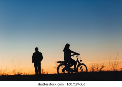 Female Cyclist On The E-bike Or Electric Bicycle On The Sunset Background. Silhouette Of The Woman And Man In Profile. Active Leisure. Travel. Sport.