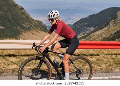 A female cyclist in red and black cycling gear rides her bike on a mountain road. She is wearing a helmet and sunglasses and is looking ahead.Sport motivation.Female cyclist wearing a cycling kit. - Powered by Shutterstock