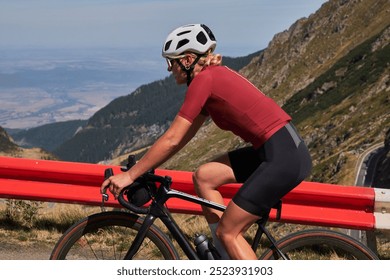 Female cyclist in a red jersey and black shorts rides uphill on a mountain road with a stunning view. Sport motivation.Female cyclist wearing a cycling kit and helmet. Carpathian Mountains, Romania. - Powered by Shutterstock