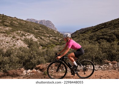 Female cyclist riding a gravel bike on a gravel road with a view of the mountains, Alicante region of Spain - Powered by Shutterstock