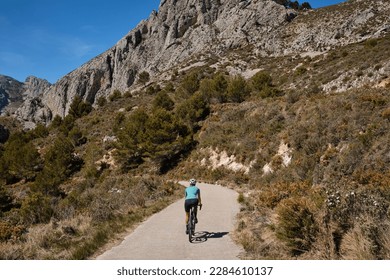 A female cyclist is training on a mountain pass on a gravel bike.Woman riding on bicycle in the mountains.Cyclist wearing a cycling kit and helmet.Gravel cycling adventure.Guadalest Reservoir,Spain. - Powered by Shutterstock