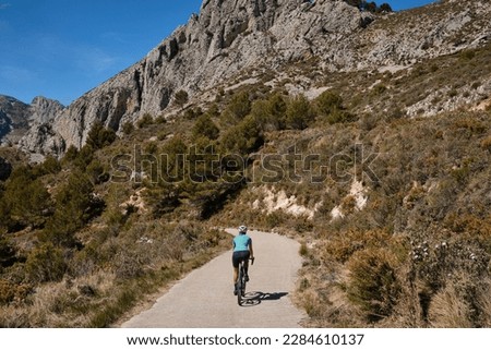 A female cyclist is training on a mountain pass on a gravel bike.Woman riding on bicycle in the mountains.Cyclist wearing a cycling kit and helmet.Gravel cycling adventure.Guadalest Reservoir,Spain. [[stock_photo]] © 