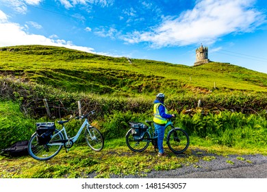 Female cyclist viewing Doonagore Castle tower outside the seaside town of Doolin, back to camera, reflective vest, helmet, blue clothing, sunny day in County Clare, Ireland. Wild Atlantic Way - Powered by Shutterstock