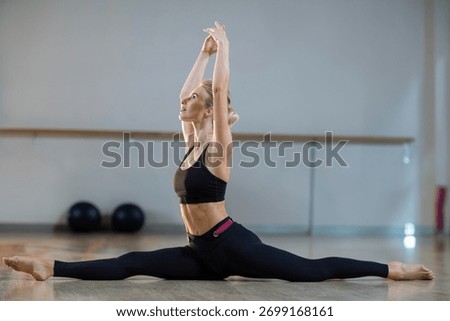 Female dancer performing split stretch on wooden floor in studio with barre and exercise balls. Flexibility, dance, fitness, athletic, movement, studio, training
