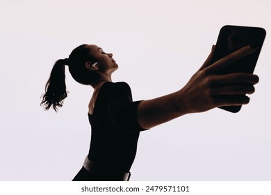 Female dancer performs dynamic dance moves with expressive body language. Listening to music on her mobile phone with earbuds in, she embodies a fit lifestyle in a studio against a white background.